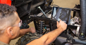 Young man in US military field uniform follows BILT 3D instructions on a tablet while working on vehicle maintenance