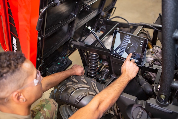 Young man in US military field uniform follows BILT 3D instructions on a tablet while working on vehicle maintenance