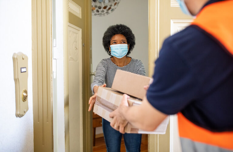 Masked woman receiving packages from a delivery man at her doorstep