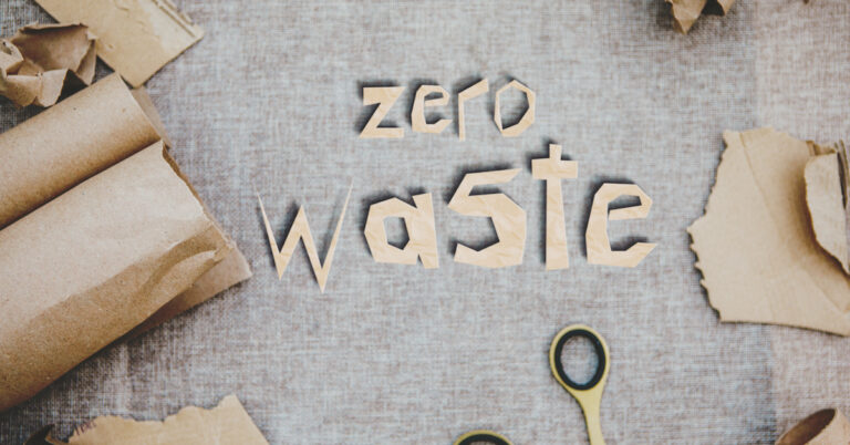 the words zero waste are cut out of cardboard and placed on a flat surface surrounded by cardboard and scissors sustainability
