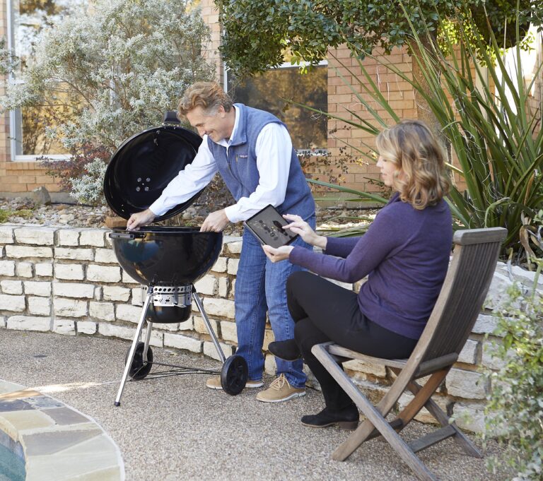 man assembles grill in back yard while woman reviews BILT 3d assembly instructions on a tablet