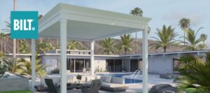 Home backyard featuring a white wooden pergola. Patio furniture and a pool in the background complete the setting.