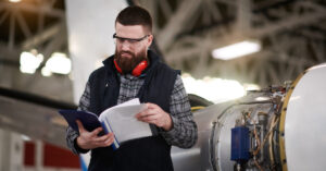 Male aircraft engineer in the hangar struggling to read instruction manuals before repairing and maintaining private jet airplane. Dyslexia affects up to 20% of the population and can impact knowledge transfer.