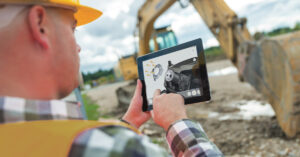 construction worker follows work instructions on a tablet using the BILT app with a backhoe in the background