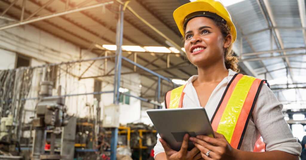 Young smiling woman holds a tablet for job training while standing in an industrial environment