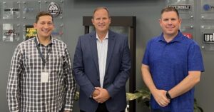 Three men stand against client logos in the BILT lobby. The men are Ahmed Qureshi, President and COO of BILT, retired Major General Cameron Holt, and Nate Henderson, Chairman and CEO of BILT