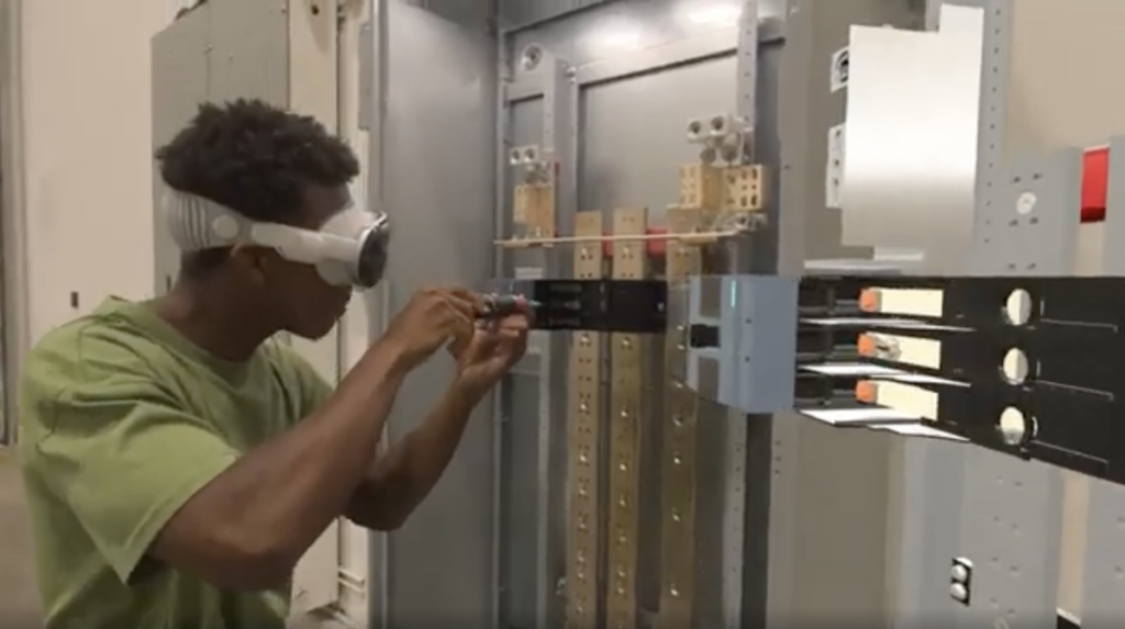 Young male training as an electrician wearing an Apple Vision Pro headset to follow virtual instructions while attaching an electric panel with a screwdriver