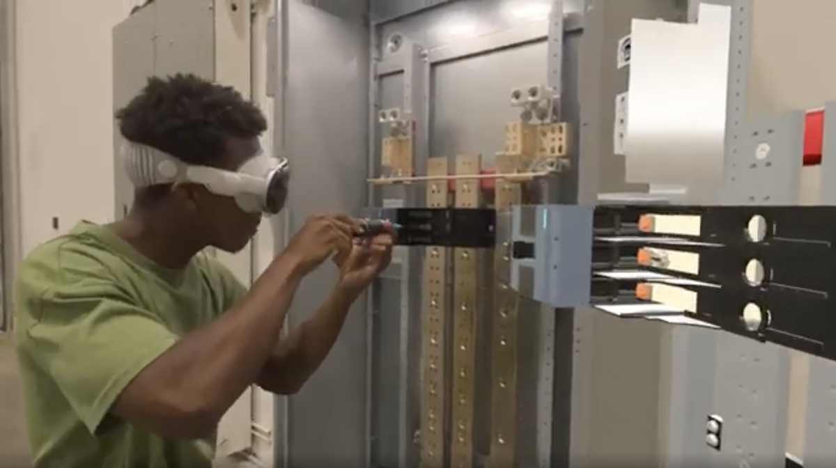 Young male training as an electrician wearing an Apple Vision Pro headset to follow virtual instructions while attaching an electric panel with a screwdriver